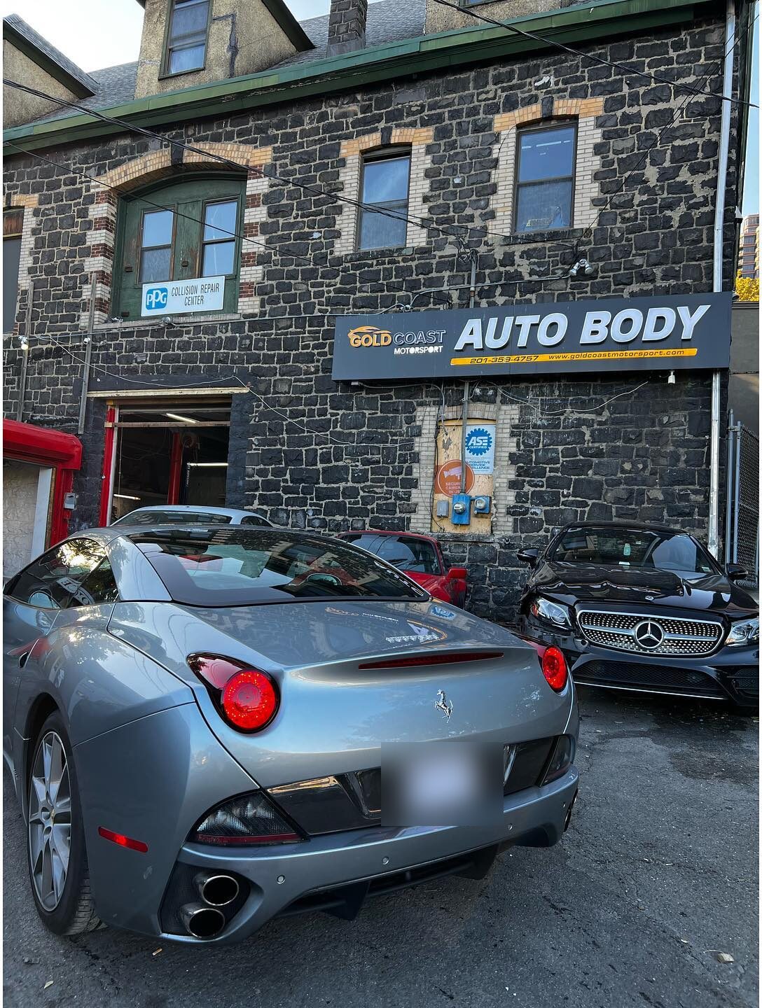 Rear three-quarter view of the silver-grey Ferrari California outside the shop, license plate blurred.